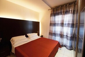 A single bed with a red bedspread in a room with a dark headboard and a striped curtain. - Residence Domus (Rimini)