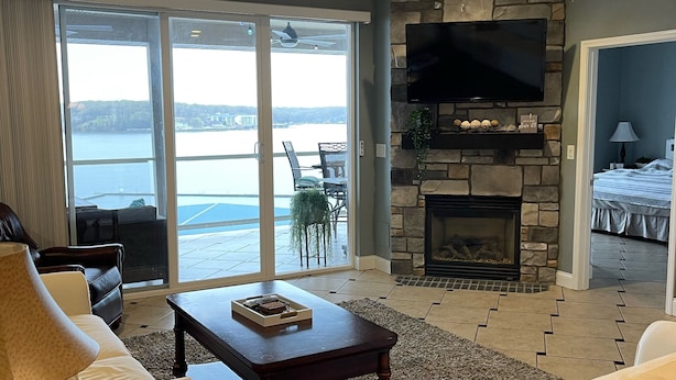 Un salon spacieux doté d’une cheminée, d’un ventilateur de plafond et d’une grande fenêtre offrant une vue sur l’eau.
