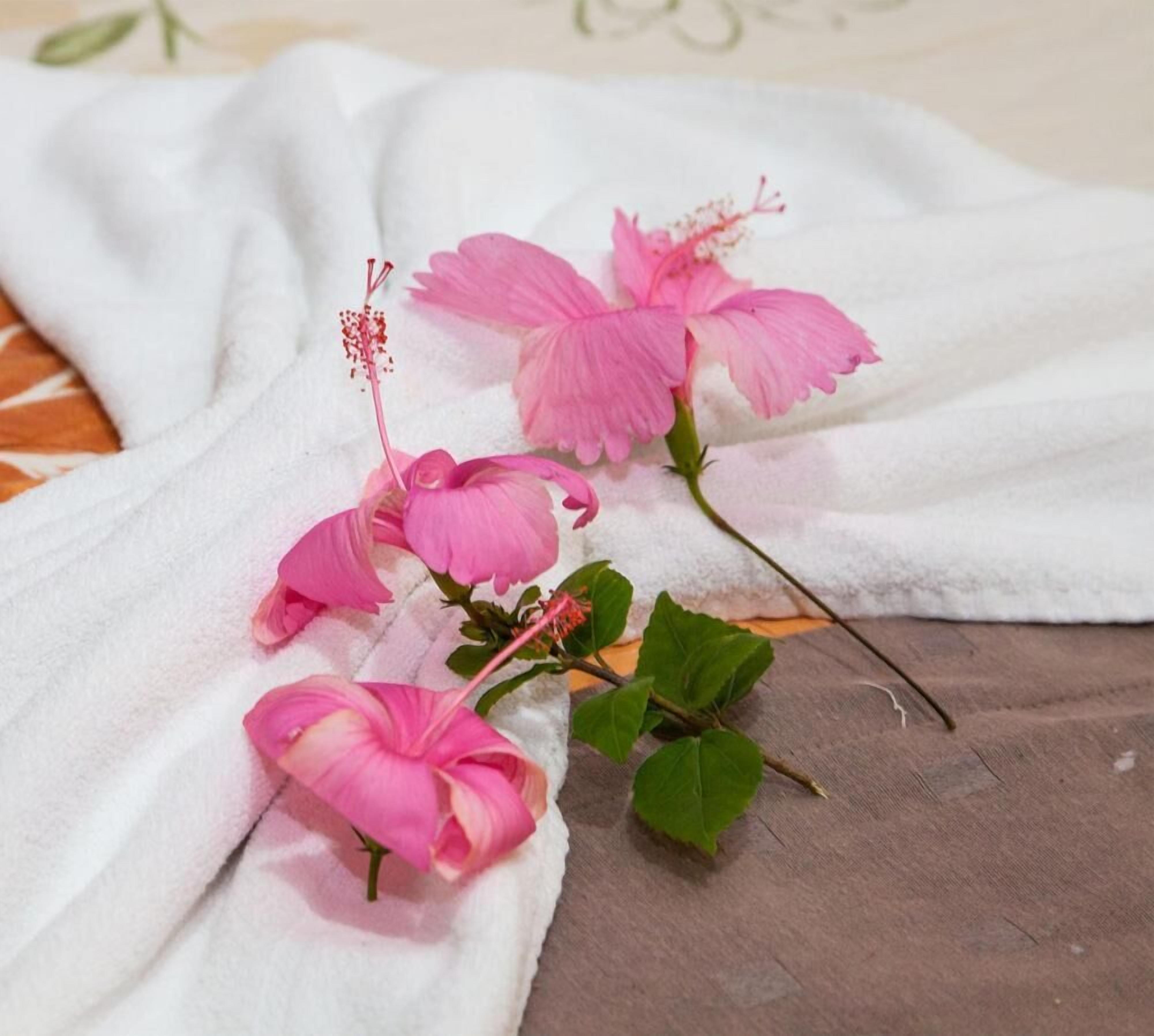 A white towel with pink hibiscus flowers and green leaves on a wooden surface.