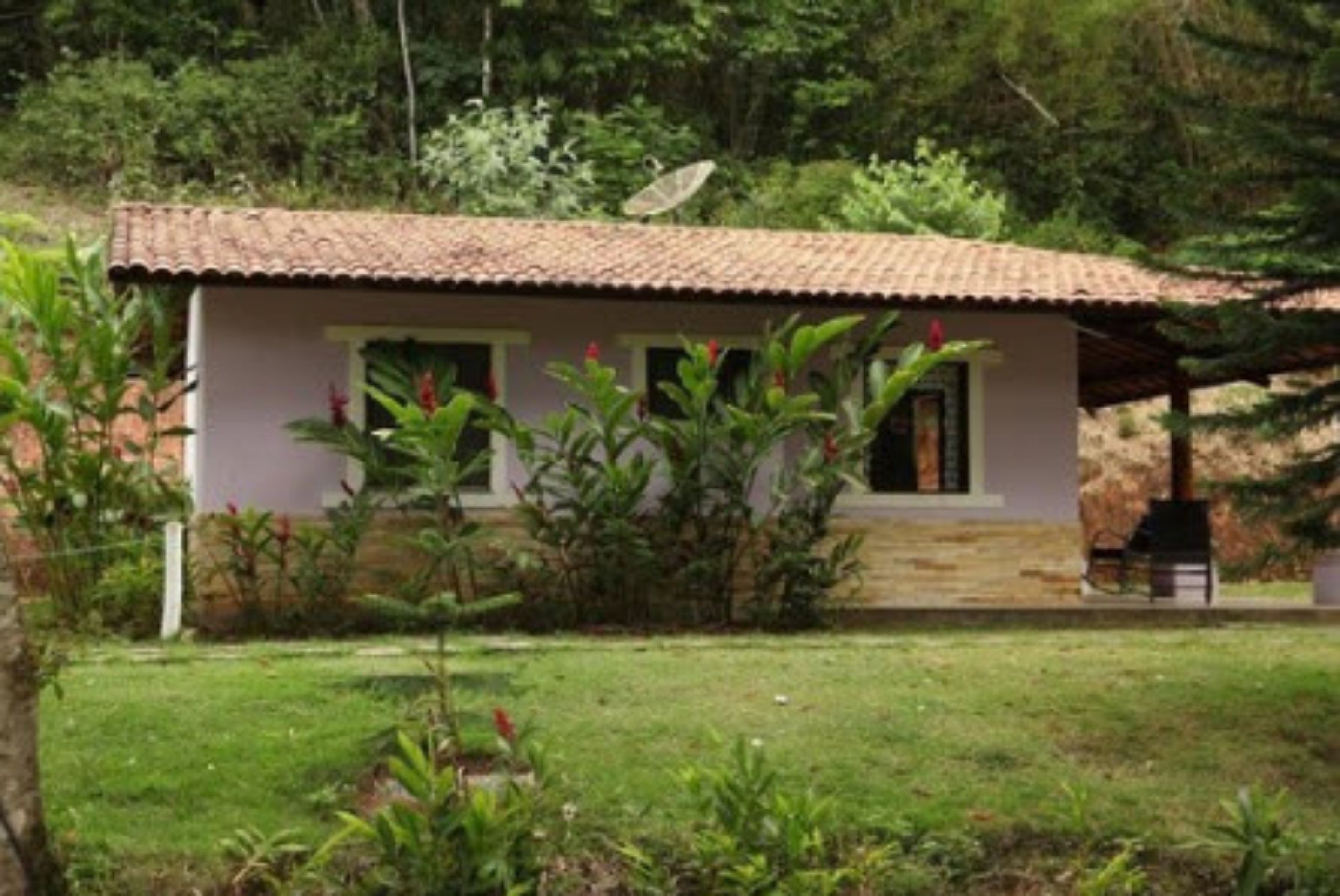 A small, single-story building with a tiled roof, surrounded by lush greenery and a well-maintained lawn.