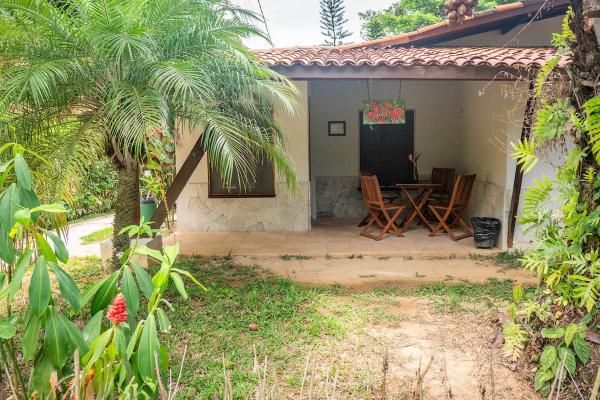 A rustic house with a tiled roof, a stone wall, and a patio with wooden furniture.