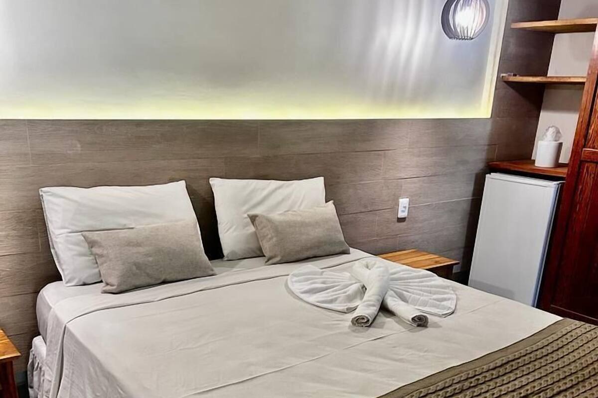 A neatly made bed with a patterned throw blanket, a towel, and a neatly folded towel on the bed.