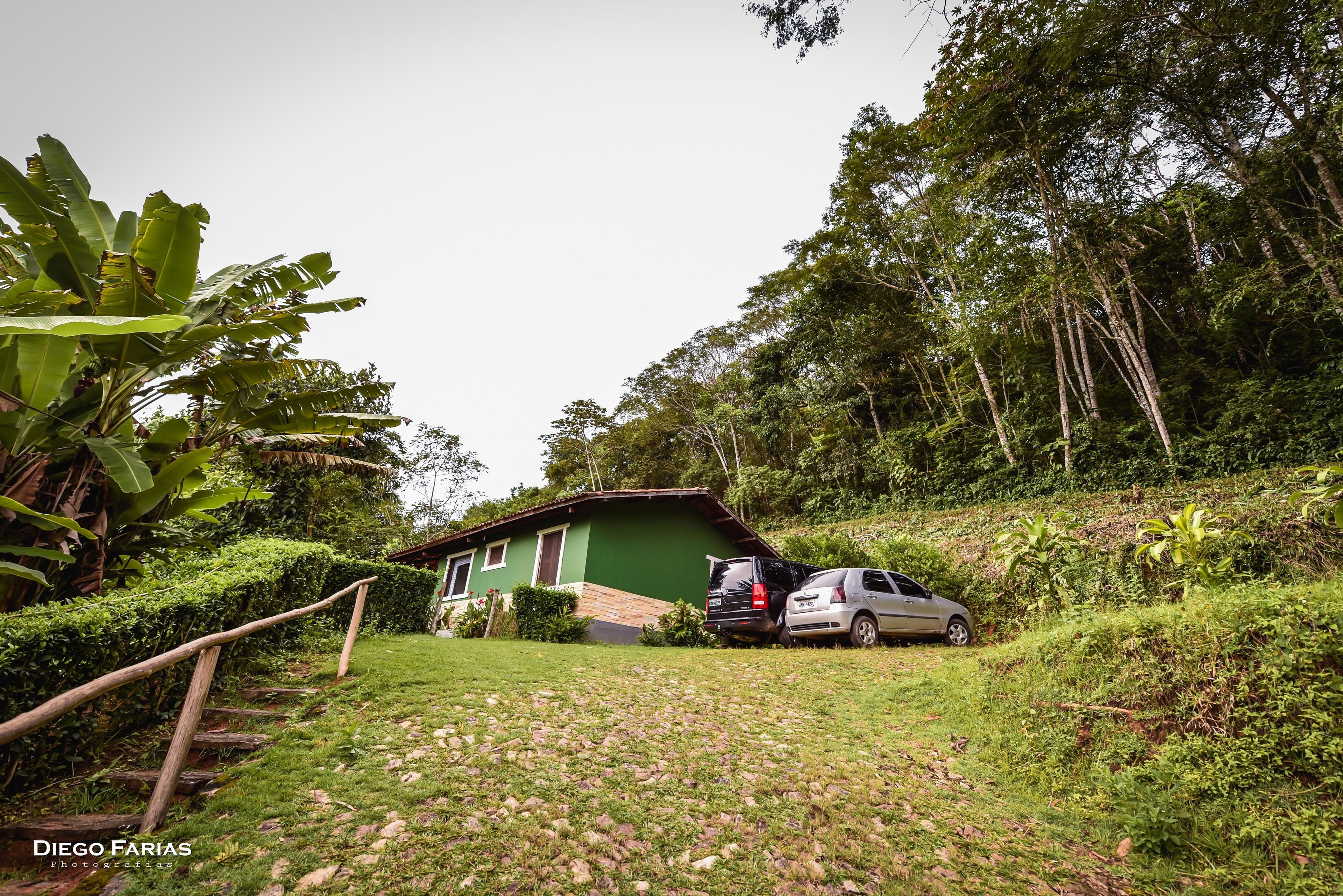 A house with a car parked in front, surrounded by lush greenery and a stone pathway.