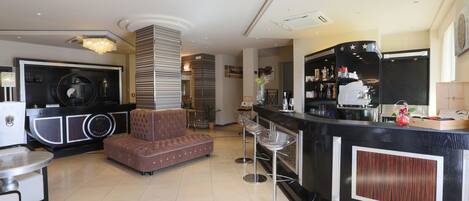Un vestíbulo de hotel con mostrador de recepción, un sofá marrón, una zona de bar con taburetes y un espejo grande.