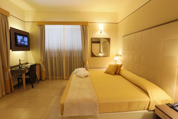 A hotel room with a bed, a desk, a chair, a television, and a window with curtains. - Hotel Milazzo (Milazzo)
