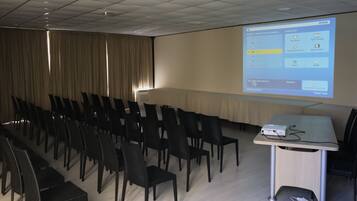Un salón de conferencias con filas de sillas, un proyector y una pantalla mostrando una presentación.