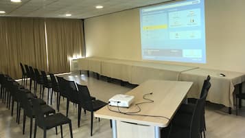 Un salón de conferencias con una pantalla de proyector mostrando una presentación, una larga mesa y varias sillas.