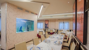 A dining area with tables set for a meal, a large aquarium, and a painting on the wall.