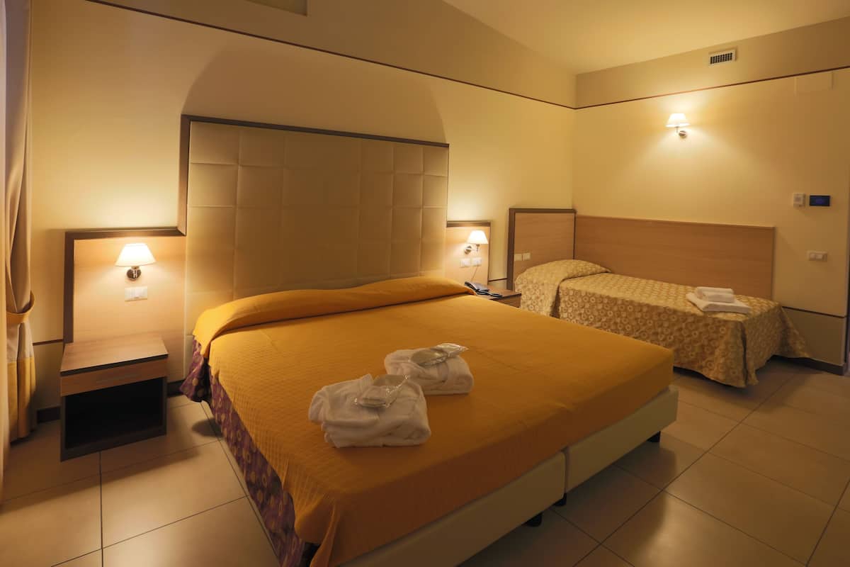 A hotel room with a large bed, a smaller bed, two bedside tables with lamps, and a headboard.