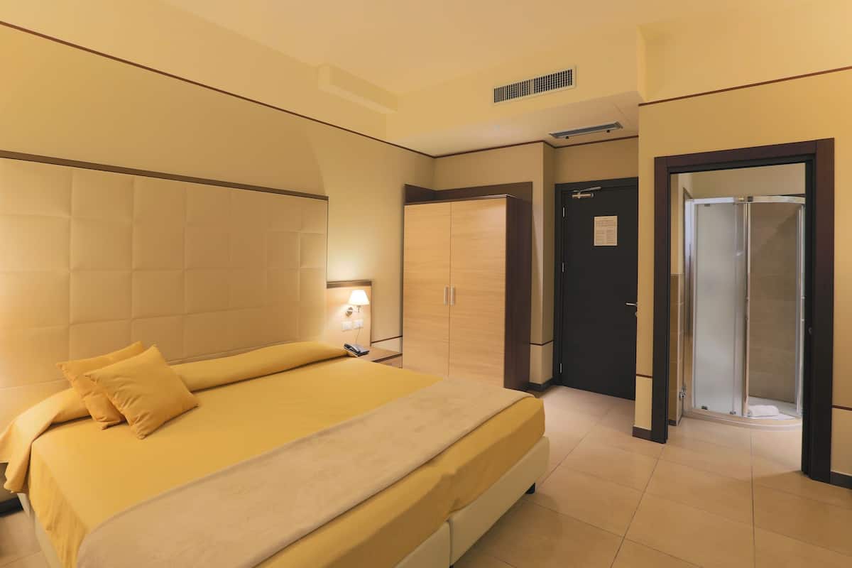 A hotel room with a large bed, a wardrobe, a bathroom with a shower, and a door leading to another room.