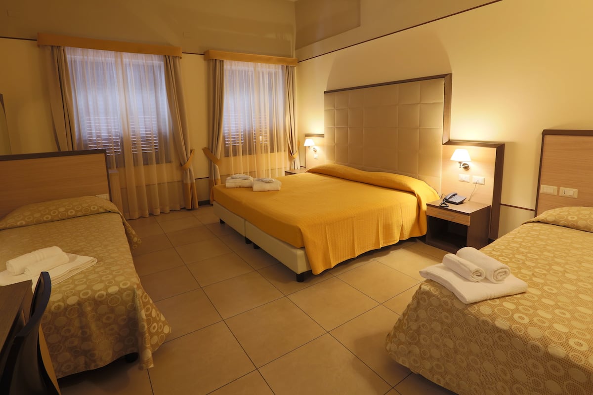 A hotel room with two beds, a nightstand, a lamp, and a window with curtains.