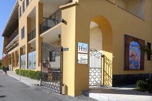 A yellow multi-story hotel with balconies, a gated entrance, and a sign indicating it is a hotel. - Hotel Milazzo (Milazzo)