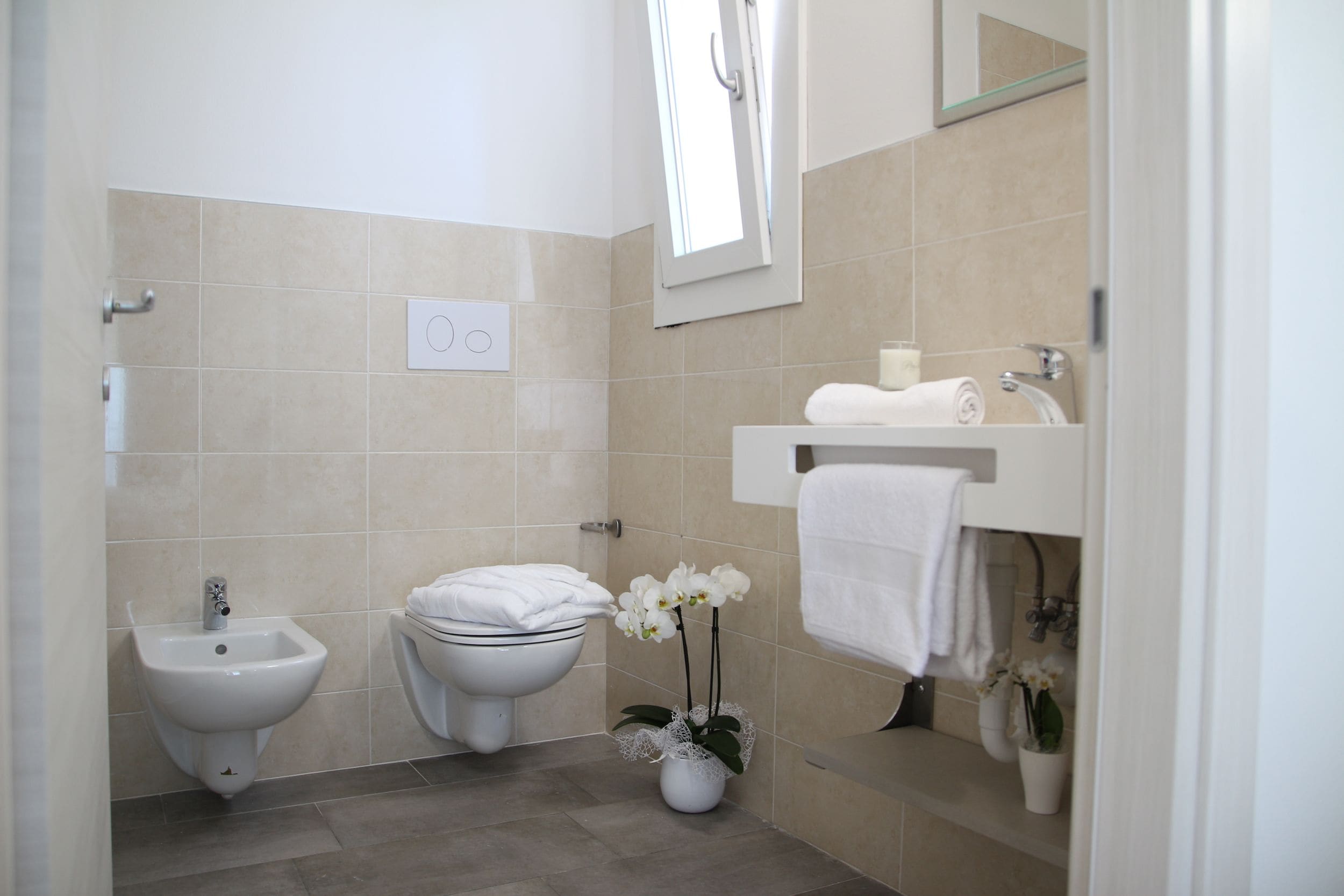 Une salle de bain moderne équipée d’un bidet, de toilettes, d’un lavabo et de deux orchidées en pot.
