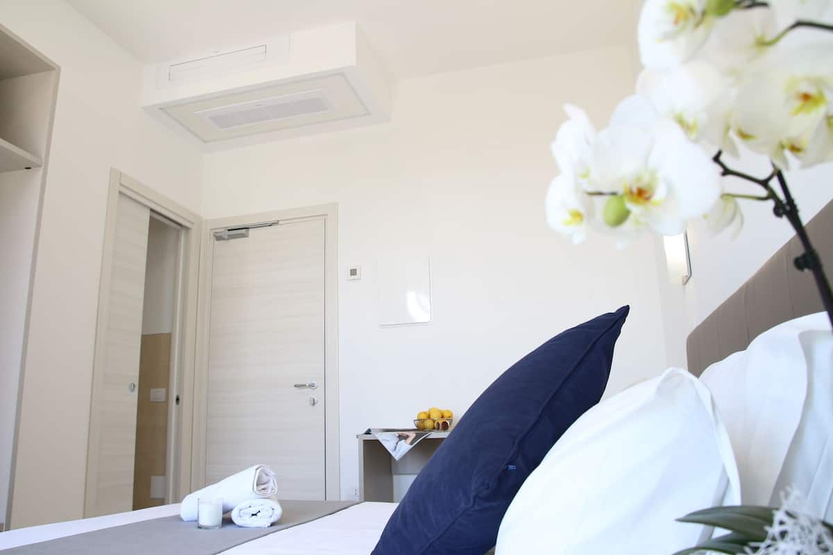 A hotel room with a bed, pillows, a bedside table with a lamp, a mirror, and a door.