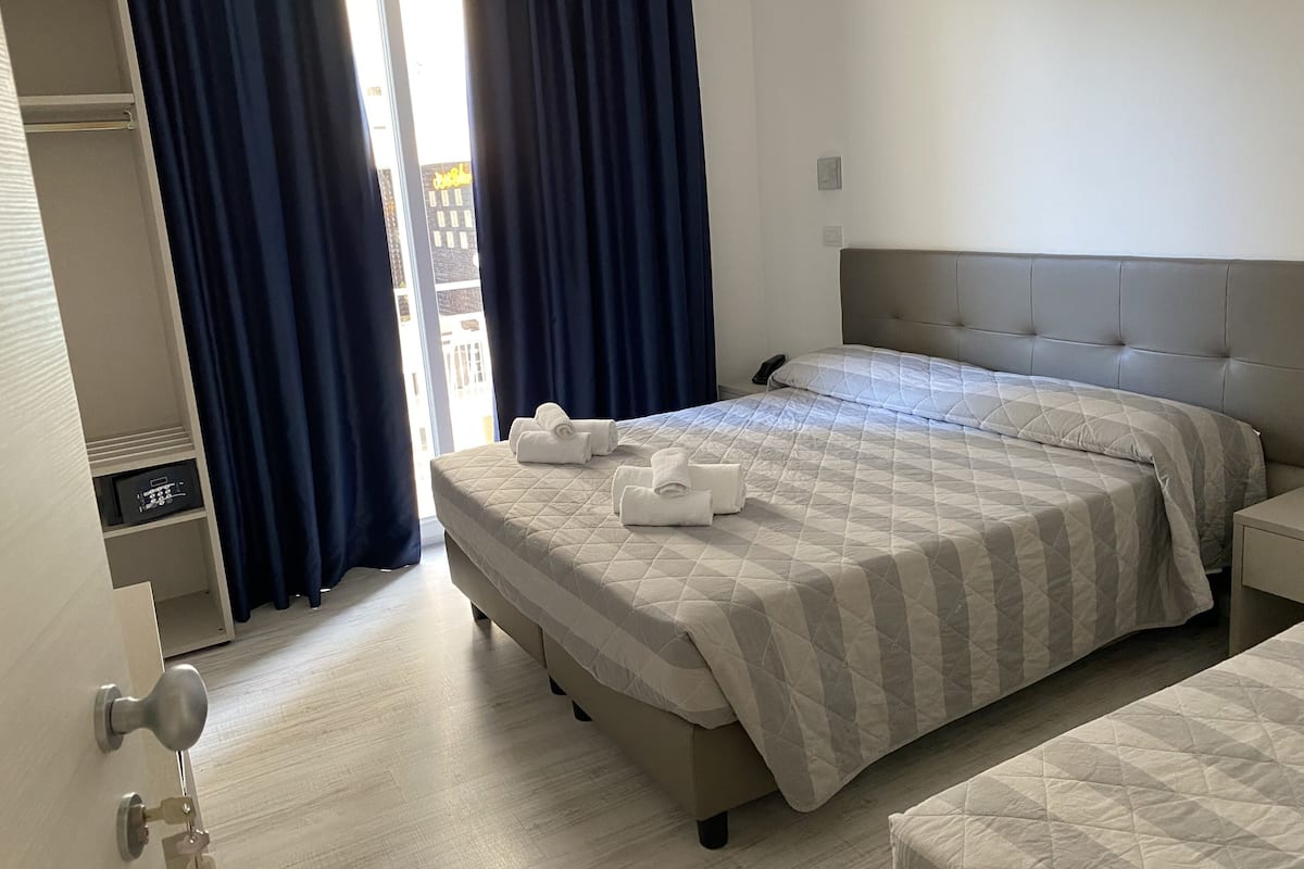 A hotel room with a bed, a bedside table, a wardrobe, and a door with a handle.