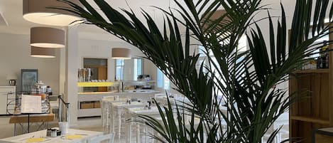 A modern dining area with white furniture, a central island, and a large potted plant.