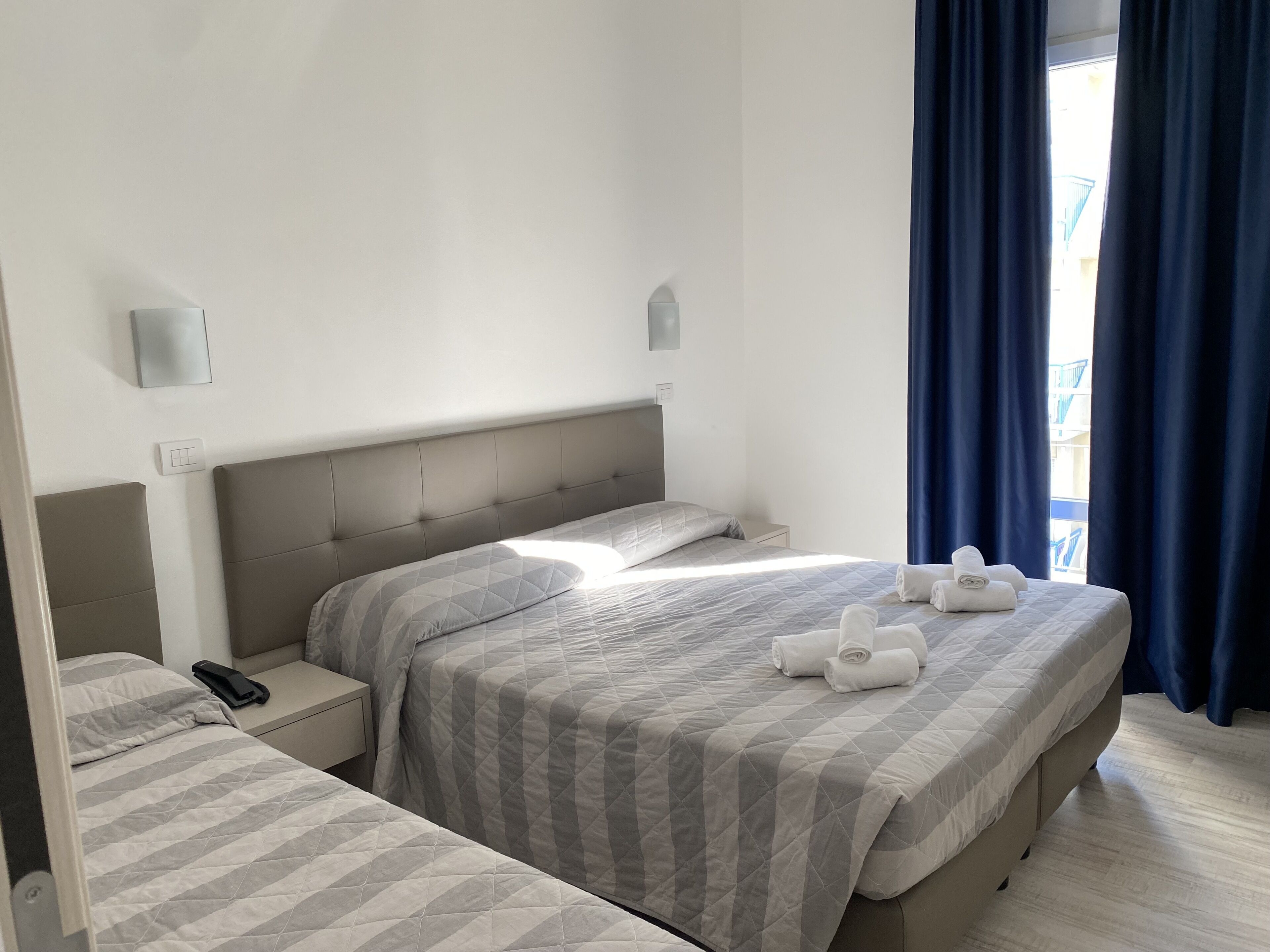 Een hotelkamer met twee bedden, een nachtkastje met een telefoon, en een raam met gordijnen.