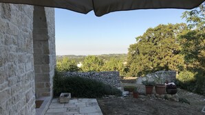 A stone wall with a stone pathway leading to a garden area with potted plants and a view of the countryside. - Original trullo on top of a hill (Locorotondo, Bari)