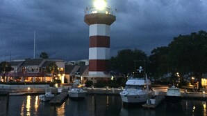 Un phare doté d’une tour rayée de rouge et de blanc, entouré d’une étendue d’eau calme où plusieurs bateaux sont amarrés.