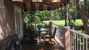 Une terrasse extérieure couverte, dotée d’une table et de chaises, et entourée d’une balustrade blanche et d’arbres.
