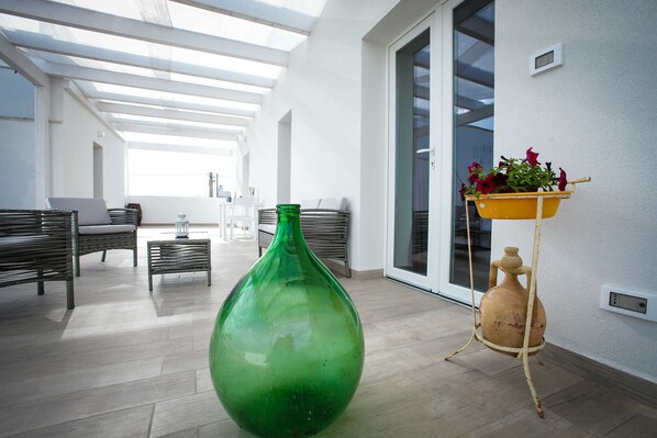Un interior moderno con un jarrón verde grande, una maceta amarilla con flores y una jarra rústica sobre un pedestal.