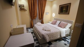 A hotel room with a bed, a bedside table, a mirror, a painting on the wall, and a window with curtains.