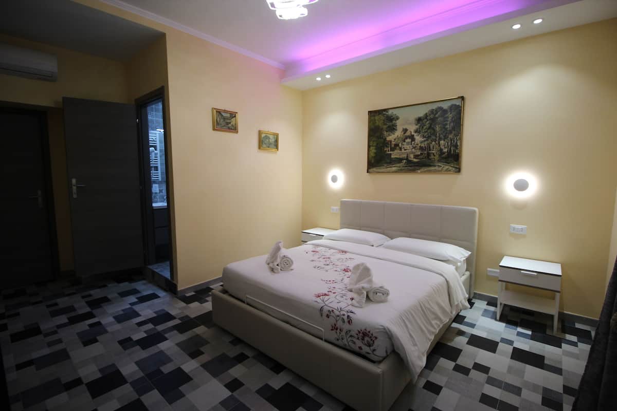 A hotel room with a bed, bedside tables, a painting on the wall, and a checkered floor.