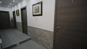 A hallway with three doors, each marked with a number. There are framed pictures on the wall and a small shelf with items.