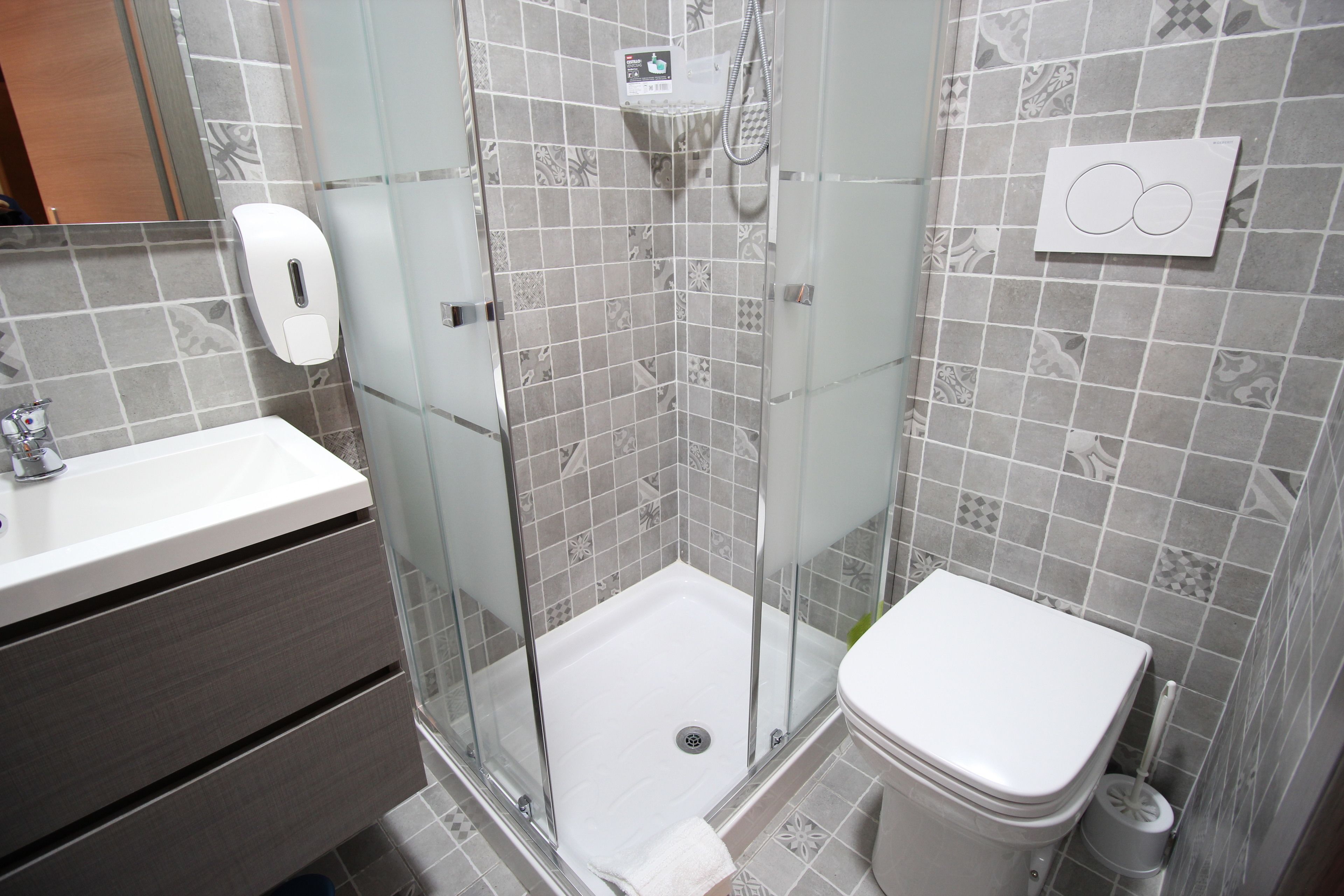 Une salle de bain moderne avec une douche à parois de verre, des toilettes et un lavabo équipé d’un distributeur de savon.