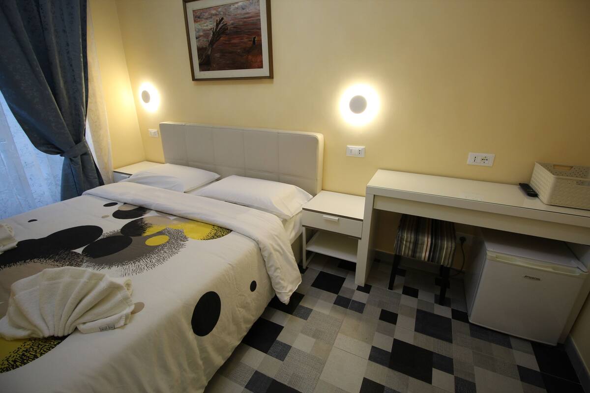 A hotel room with a bed, bedside table, and a desk with a chair.