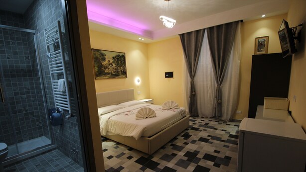 A hotel room with a bed, a shower, a small desk, and a mirror.