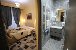 A hotel room with a bed, a bedside table, a mirror, and a bathroom with a sink and towel rack. - Quest House Lihong (Rome)