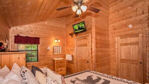 A wooden cabin bedroom with a bed, a vanity, a television, and a ceiling fan. - Absolutely Bearable: S/Secluded, Honeymoon, Hot Tub, Games, near Attractions! (Sevierville)