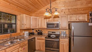 A kitchen with wooden cabinets, stainless steel appliances, granite countertops, and a window. - Absolutely Bearable: S/Secluded, Honeymoon, Hot Tub, Games, near Attractions! (Sevierville)