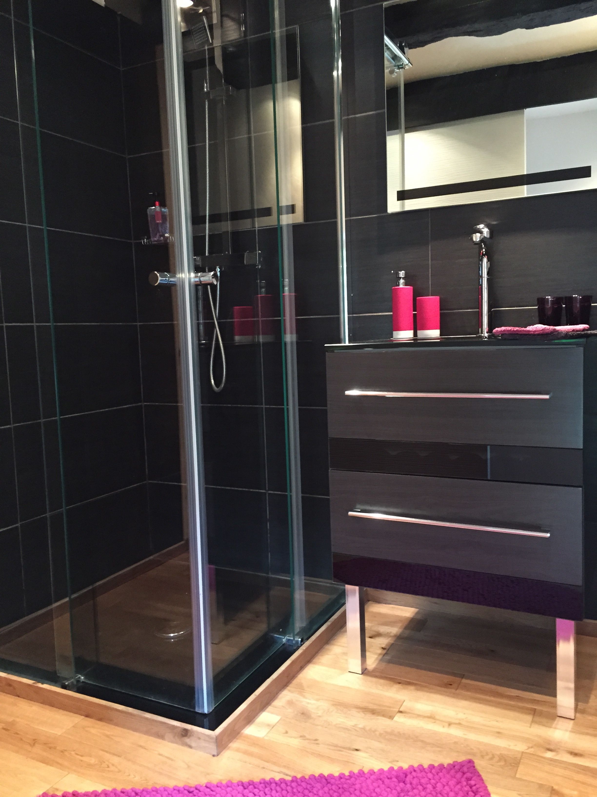 A modern bathroom with a glass-enclosed shower, a black vanity with a mirror, and a wooden floor.