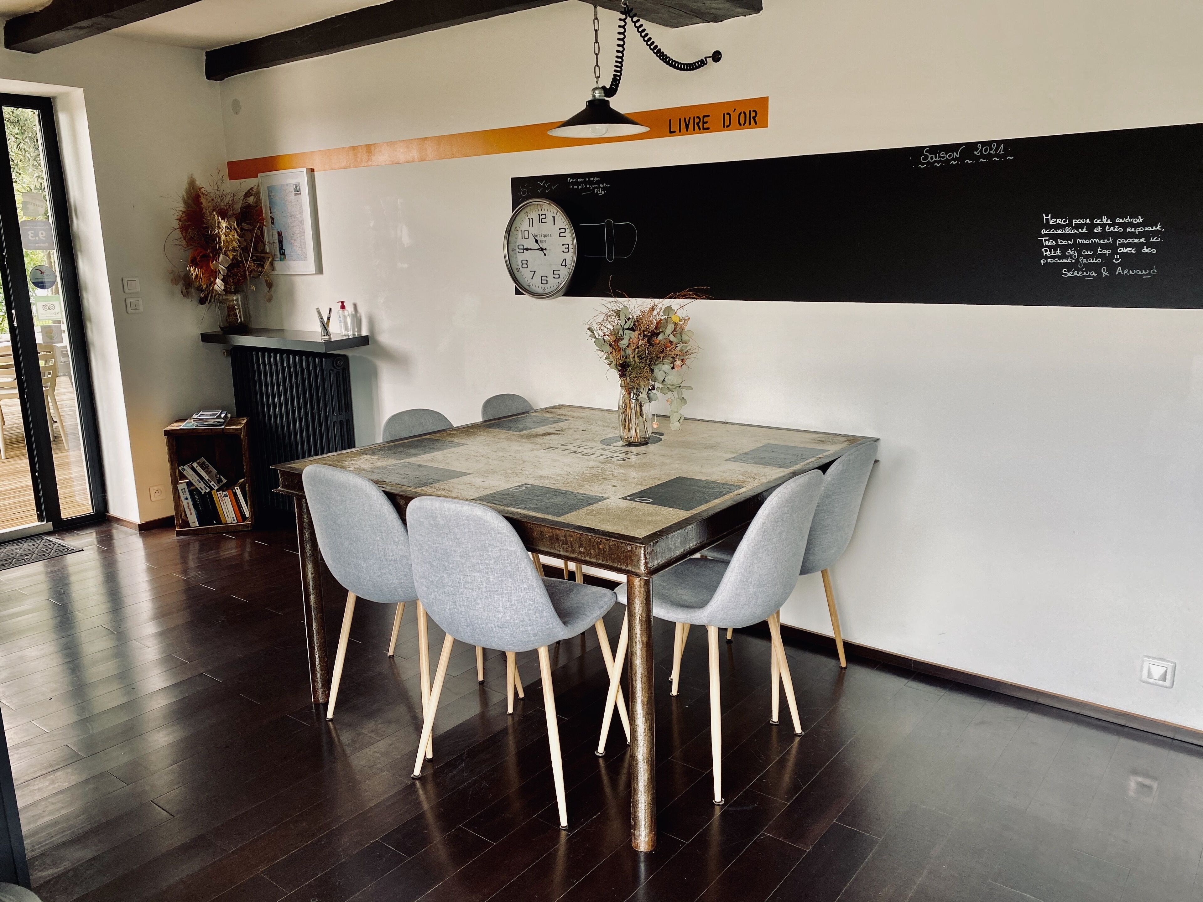 Un comedor con mesa de madera, sillas grises, un reloj y un jarrón decorativo.