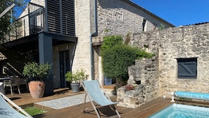 A poolside area with a wooden deck, two lounge chairs, and a stone wall. - Ô Chambre d'hôtes (Le Gua)