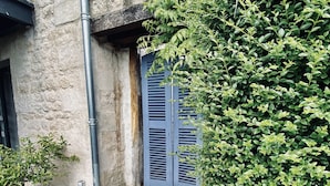 A courtyard with a tiled floor, a potted plant, a blue door, and a stone wall. - Ô Chambre d'hôtes (Le Gua)