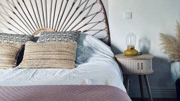 A bed with a unique bamboo headboard, a bedside table with a lamp, and a vase with pampas grass.