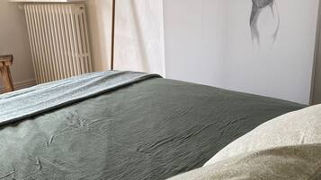 A bedroom with a bed, a radiator, a wall with a drawing, and a shelf with items.