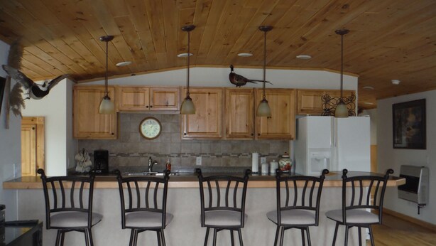 A kitchen with wooden cabinets, a central island with bar stools, a clock, and a refrigerator.