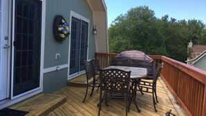 A wooden deck with a covered barbecue table and chairs, a wicker wreath, and a sliding glass door.
