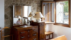Ein Holzkommode mit Schubladen, ein Spiegel und eine Lampe. Draußen befindet sich ein Fenster mit einem Metallgitter.
