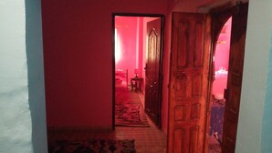 Un couloir avec une porte en bois et un tapis menant à une pièce dont un mur est rose et qui contient un lit.