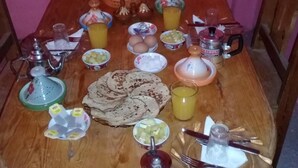 Une table de salle à manger en bois, dressée avec divers aliments pour le petit-déjeuner, notamment des œufs, du pain et des boissons.