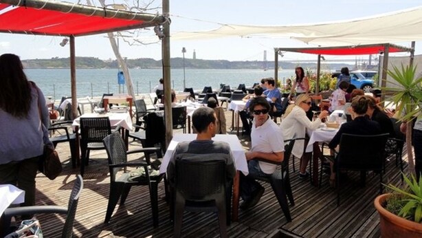 An outdoor dining area with tables and chairs, overlooking a body of water with a bridge in the background. - NEW HOUSE DESIGN, TYPICALISBON (Lisboa)