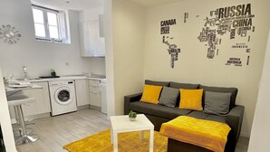 A modern apartment with a kitchen, a living area with a sofa and cushions, and a small white table. - NEW HOUSE DESIGN, TYPICALISBON (Lisboa)
