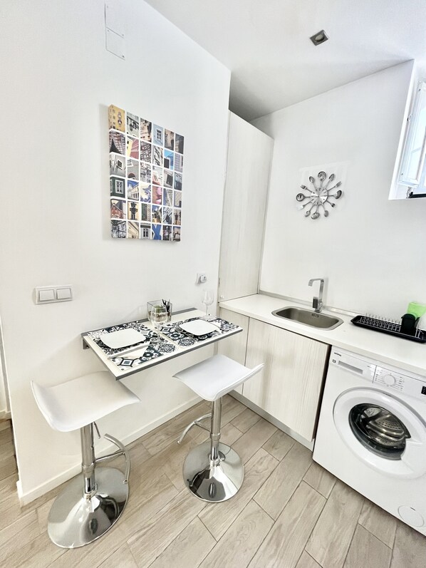 A compact kitchen with a washing machine, a tiled backsplash, and a wall-mounted utensil holder.