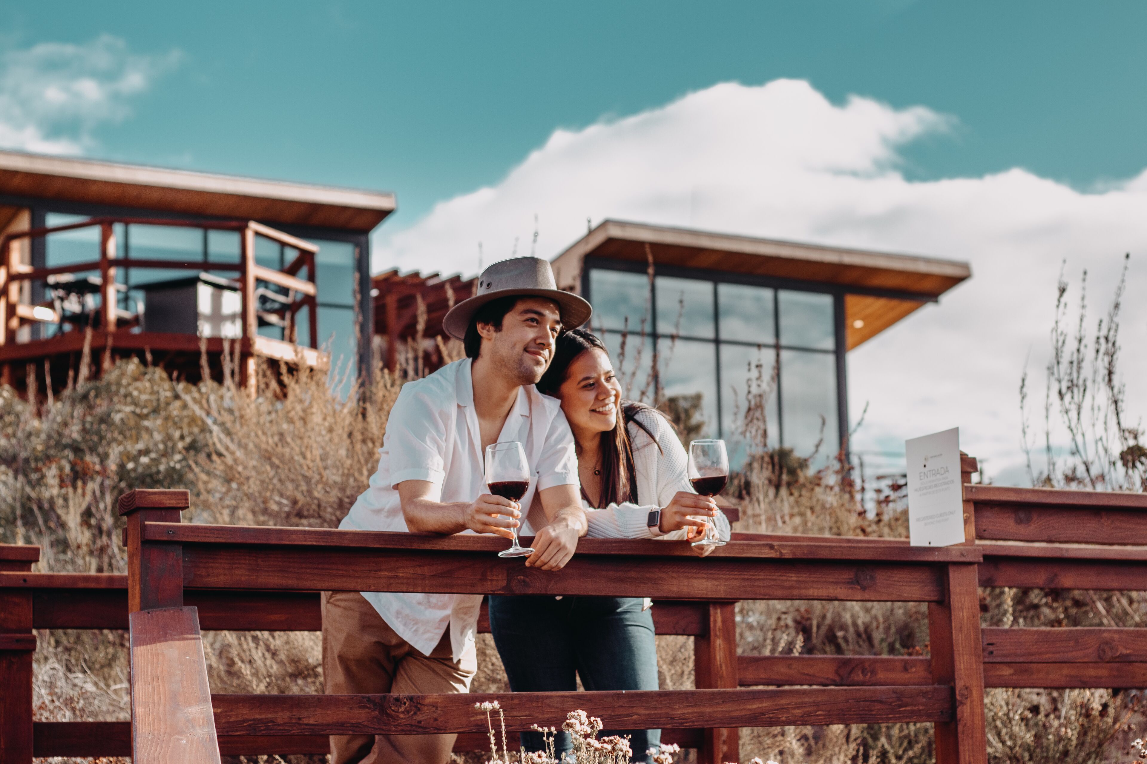 A couple sitting on a wooden bench with a modern building in the background.