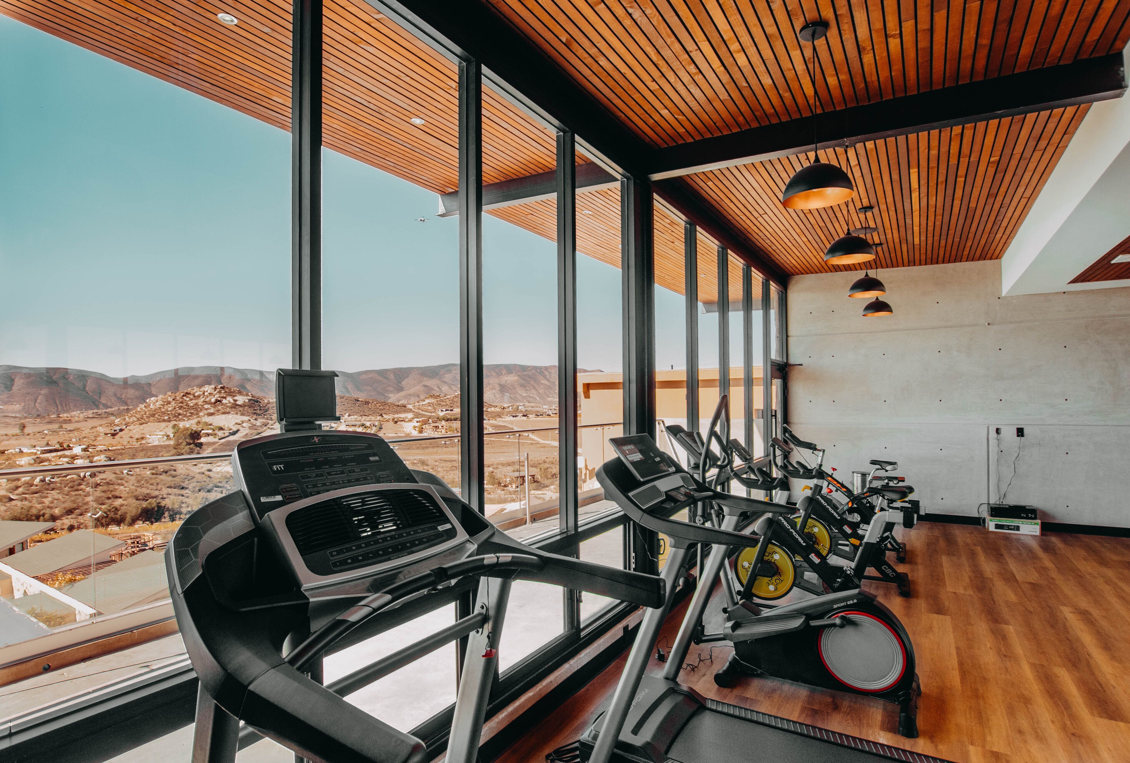 Un gimnasio con equipamiento de ejercicio y amplias ventanas que ofrecen vistas a un paisaje desértico.